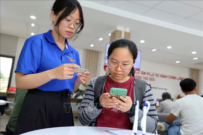 青年志愿者在胡志明市守德坊公共行政服务中心帮助人们使用智能手机申报和提交资料。图自越通社