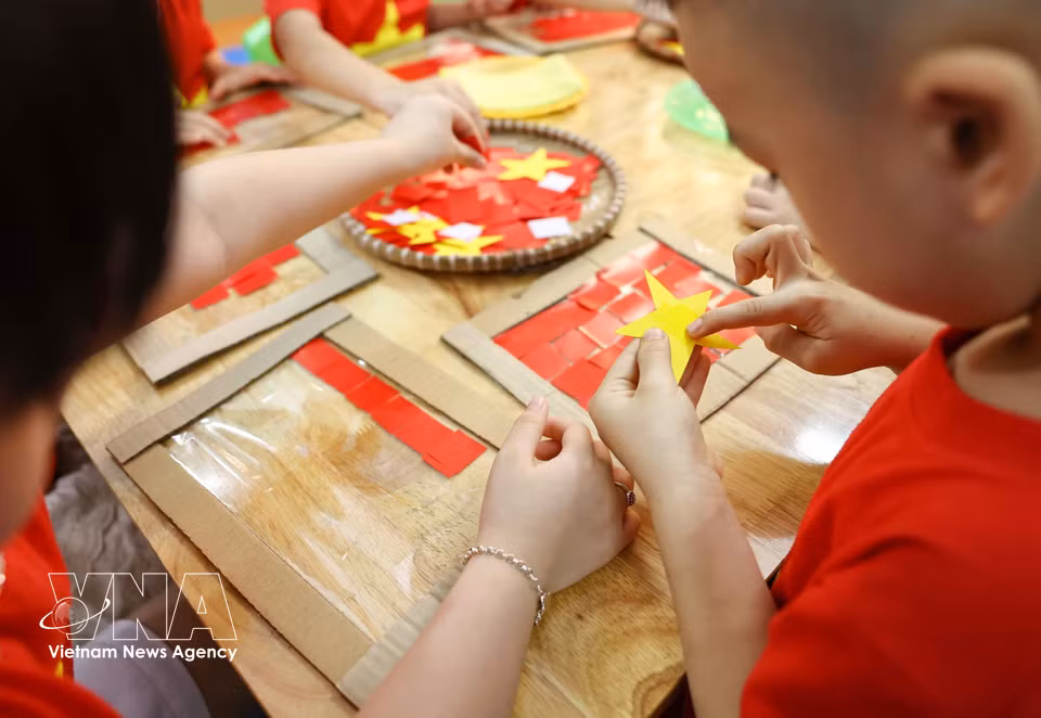 幼儿们细心剪贴，完成鲜艳而充满爱意的祖国国旗作品。图自 越通社