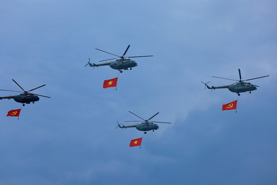 直升机悬挂越南共产党党旗、国旗，飞过礼台。图自 越通社