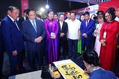 越南政府总理范明政、越共中央总书记苏林夫人吴芳璃和各位代表欣赏书法大师展示才艺。图自越通社