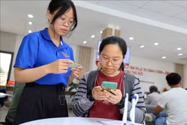 青年志愿者在胡志明市守德坊公共行政服务中心帮助人们使用智能手机申报和提交资料。图自越通社