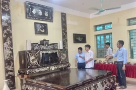 专美社手工艺人向游客介绍其家族价值30多亿越盾的螺钿镶嵌及磨漆榻床、橱柜和横披对联。图自越通社