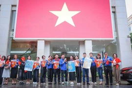 越南通讯社青年团在总部与大型国旗合影留念。图自 越通社