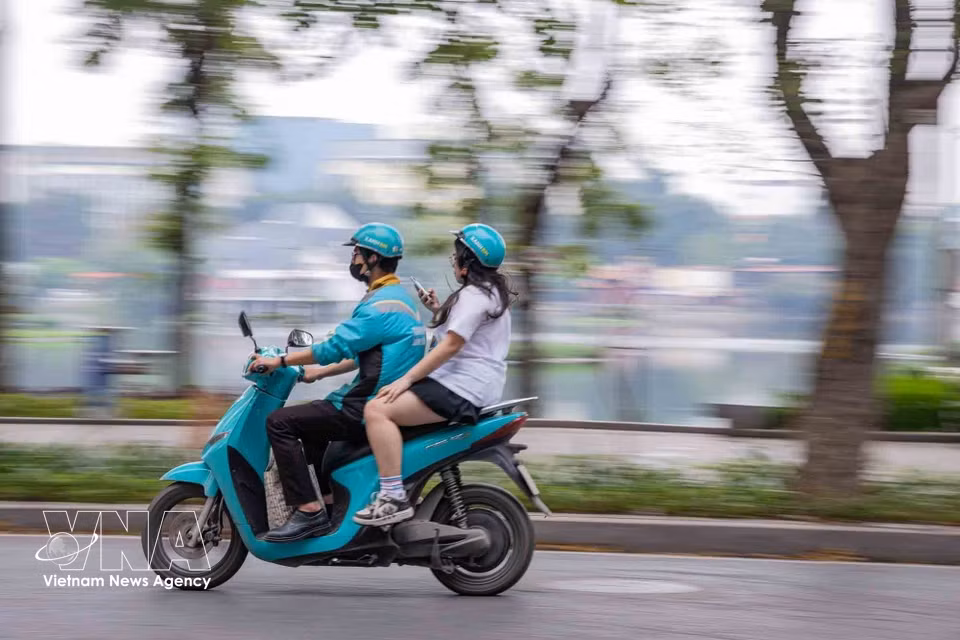一名网约车司机骑着电动摩托车在河内阮攸街上载客行驶。图自越通社