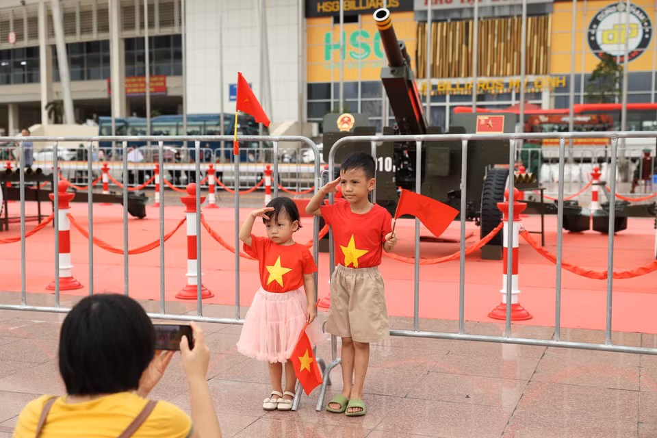 孩子们在父母的带领下，手持国旗与礼炮合影。图自越通社