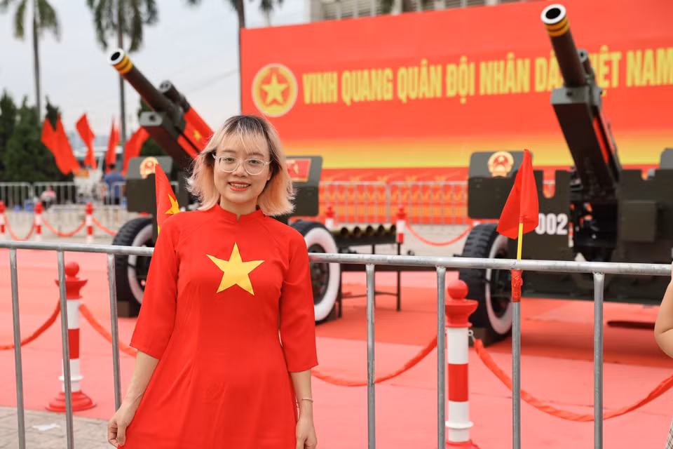 站在礼炮旁的一名身穿着印有国旗图案的传统奥黛的青年笑容灿烂迎国庆。图自越通社