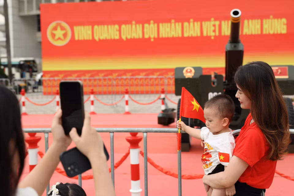 孩子们在父母的带领下，手持国旗与礼炮合影。图自越通社