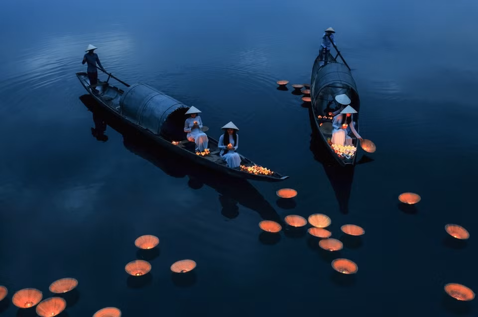 摄影师裴富庆的摄影作品《祈祷》。作者拍摄身上穿着奥黛、头上戴着斗笠的越南姑娘在江边放花灯，为逝者祈福的景色。图片来源：vnexpress.net