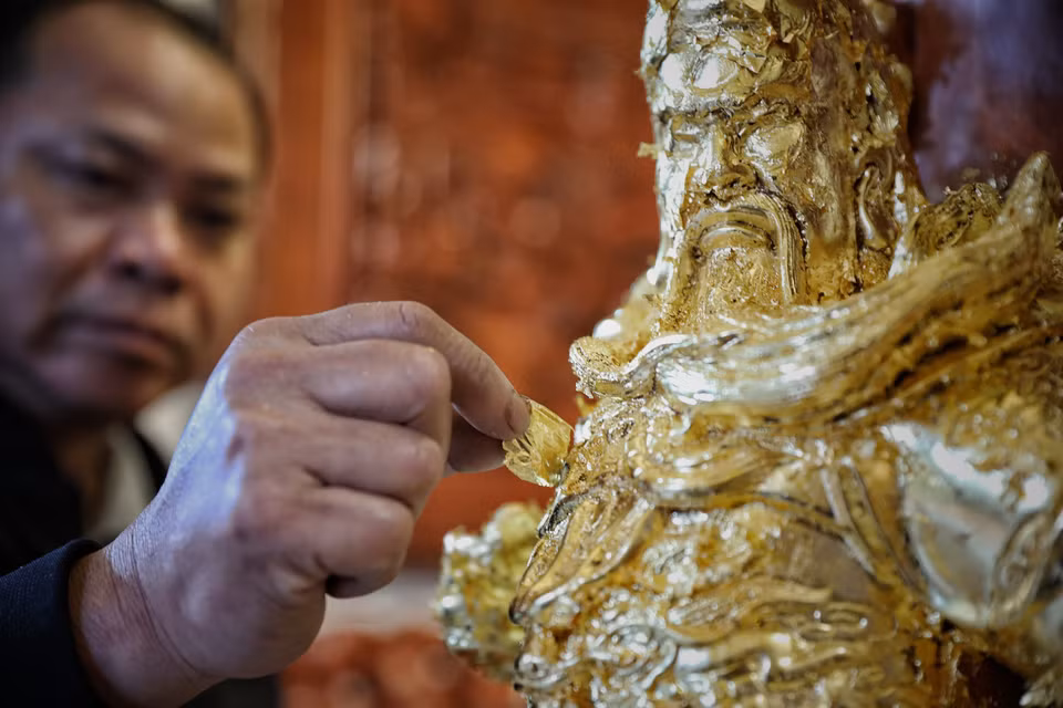 阮英钟艺人细心地把金箔粘贴在雕像上。图自越通社