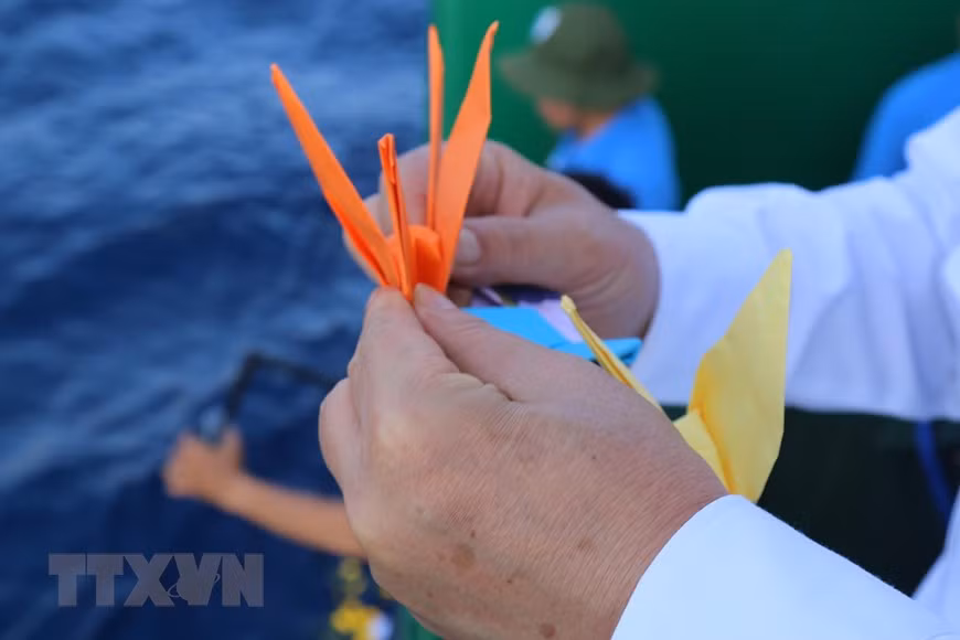 长沙571号船的干部战士向海里放纸鹤，缅怀在长沙群岛海域牺牲的英雄烈士。图自越通社