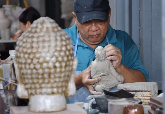 与陶器制作业结伴30年的黎青赝艺人正在制作一尊陶瓷佛像。图自越通社