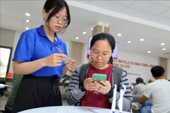 青年志愿者在胡志明市守德坊公共行政服务中心帮助人们使用智能手机申报和提交资料。图自越通社
