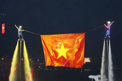 表演者在同奈河上进行高空升旗表演，越南国旗迎风飘扬。图自 越通社