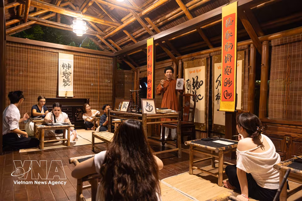 国内外游客在文庙-国子监的“精华道学”夜间体验之旅中，于“夫子屋”空间参加书法体验课。图自越通社