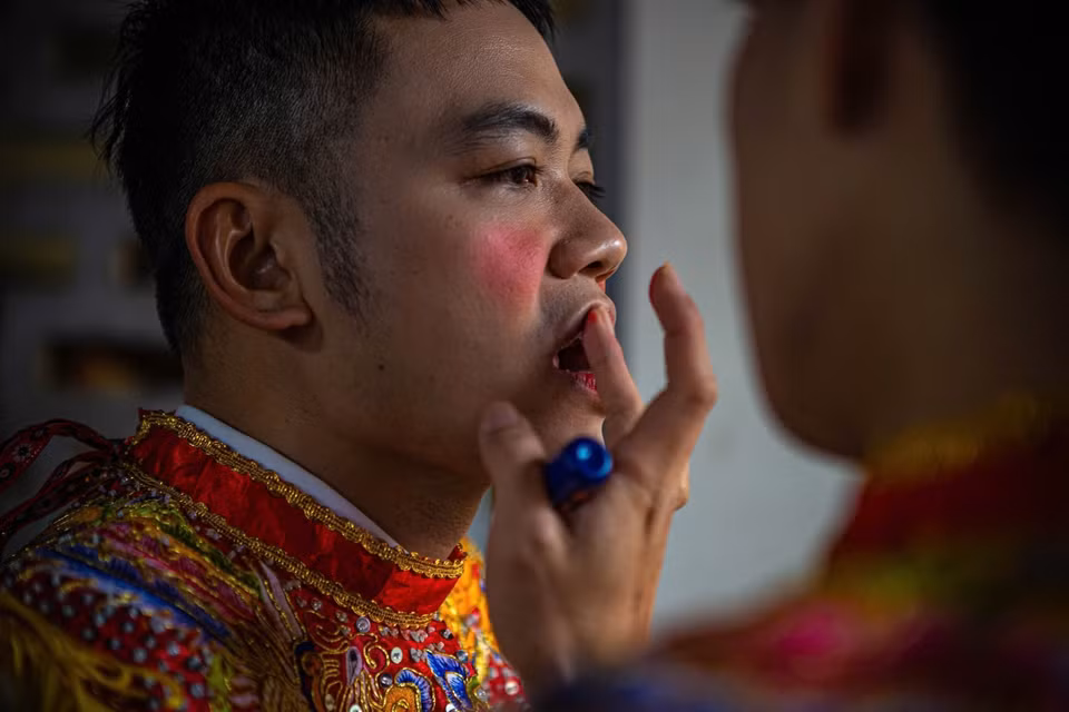 朝曲村腰鼓俱乐部成员涂上胭脂、男扮女装，准备参加腰鼓舞表演。图自越通社