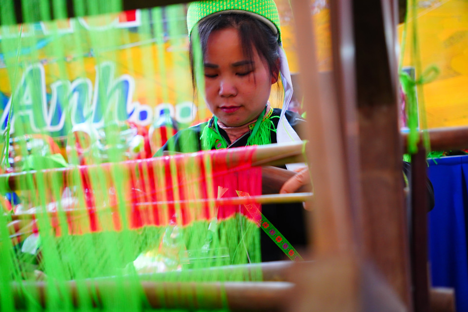 谅山省展区内，身着侬族传统服饰的妇女正展示传统纺织技艺。图自越通社