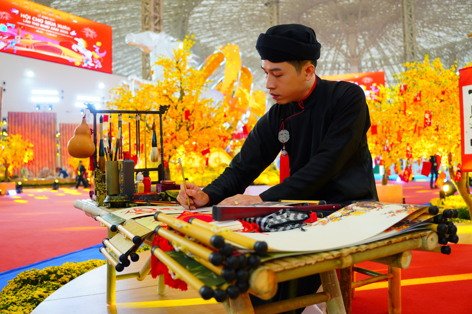 身着男士奥黛、卷边巾的手艺人展示书法艺术。图自越通社