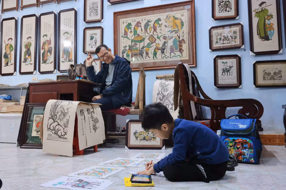 作为东湖画第13代传人，优秀工匠阮有果欣慰地看到孙子阮有明灯正使用古老的东湖画框进行创作。图自越通社