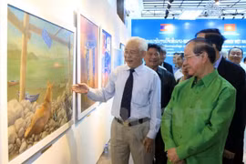 越南美术协会主席陈庆章（左）向老挝代表团介绍展会中的图片。
