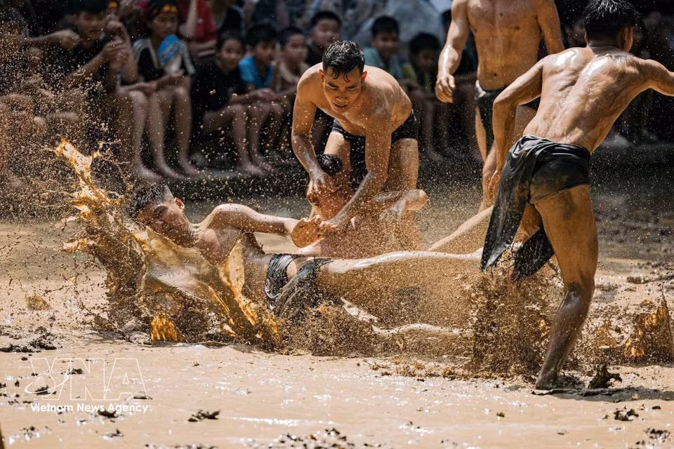 一名选手在激烈碰撞后摔倒在泥地中央，而队友和对手仍紧追木球继续争夺。图自越通社