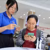 青年志愿者在胡志明市守德坊公共行政服务中心帮助人们使用智能手机申报和提交资料。图自越通社