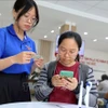 青年志愿者在胡志明市守德坊公共行政服务中心帮助人们使用智能手机申报和提交资料。图自越通社
