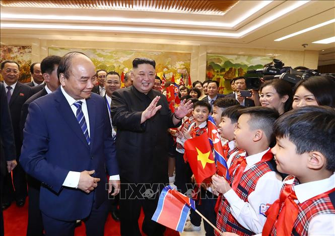 阮春福和金正恩向挥舞越朝两国国旗的孩子们挥手致意。图自越通社