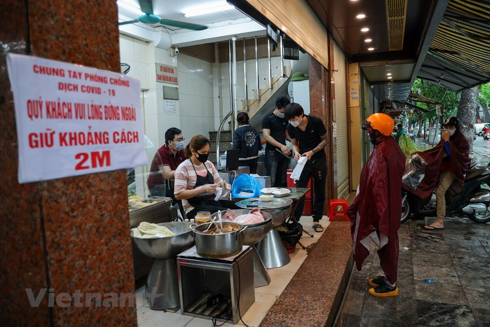  社交距离措施放宽后，人们逐步进入“新常态”，做了“与新冠肺炎疫情共处”的心理准备。人们习惯出门时佩戴口罩，勤洗手，外出吃饭时优先选择带走方式，以限制与多人接触，避免感染新冠病毒，进而控制疫情扩散蔓延。图中的这家早餐店还提醒食客保持2米的安全距离。Vietnam+记者 明山 摄