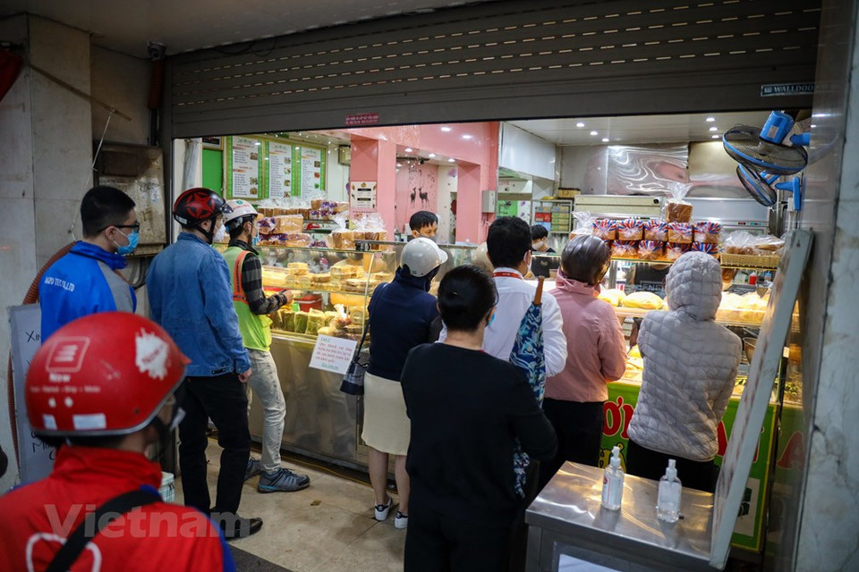  一家跨国市场研究公司对15个国家的公民展开了有关是否相信社交距离措施结束后国家经济将快速复苏的调查。80%的越南受访者相信经济将在社交距离措施结束后快速复苏，名列受访15个国家名单中前茅。图为：河内市金马街上一家著名面包店很早就开门，很多人在排队等待购物。Vietnam+记者 明山 摄