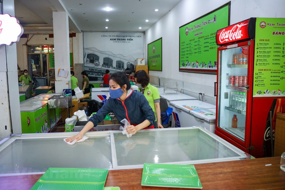  河内市人民委员会主席阮德钟强调，虽然放宽社交距离措施，但酒吧、电子游戏店以及街头茶水摊等仍暂停营业，禁止举行聚集性活动等。4月23日正式放宽社会距离措施的第一天。各家商店可以重新开门。图为：河内市长前冰淇淋店服务员打扫店里卫生，进行消毒，准备迎客。Vietnam+记者 明山 摄