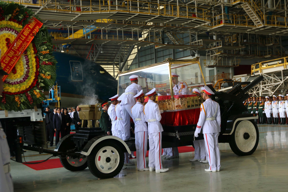 护灵的军人仪仗队将灵柩从飞机搬下来,送入等候在一边的灵车。图自越通社