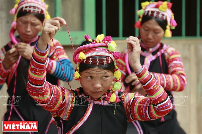 首先，她们将头发分中缝，用红棕色塑料圈固定。其次，系上缀着白色小串珠的绣花布巾。图自 越通社/越南画报