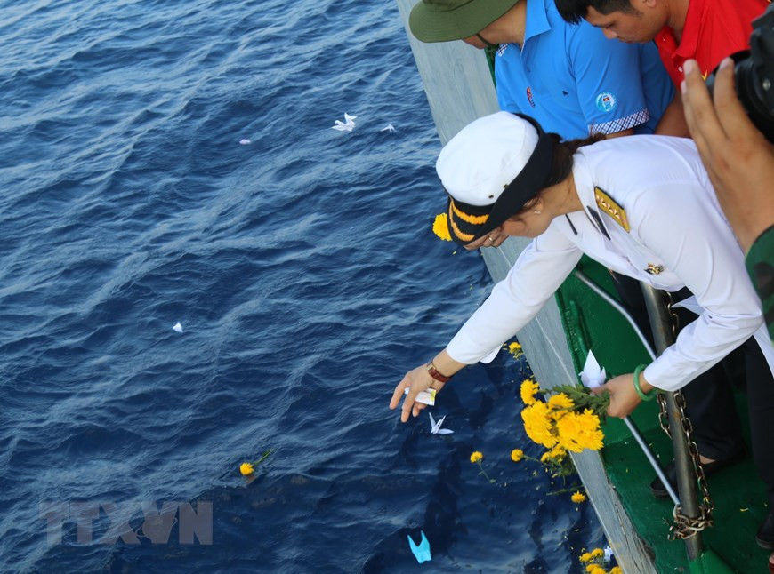 在长沙群岛上牺牲的武装力量英雄烈士陈文方的女儿陈氏水上尉从长沙571号船向海里撒花瓣，以缅怀英雄烈士。图自越通社