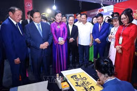 越南政府总理范明政、越共中央总书记苏林夫人吴芳璃和各位代表欣赏书法大师展示才艺。图自越通社