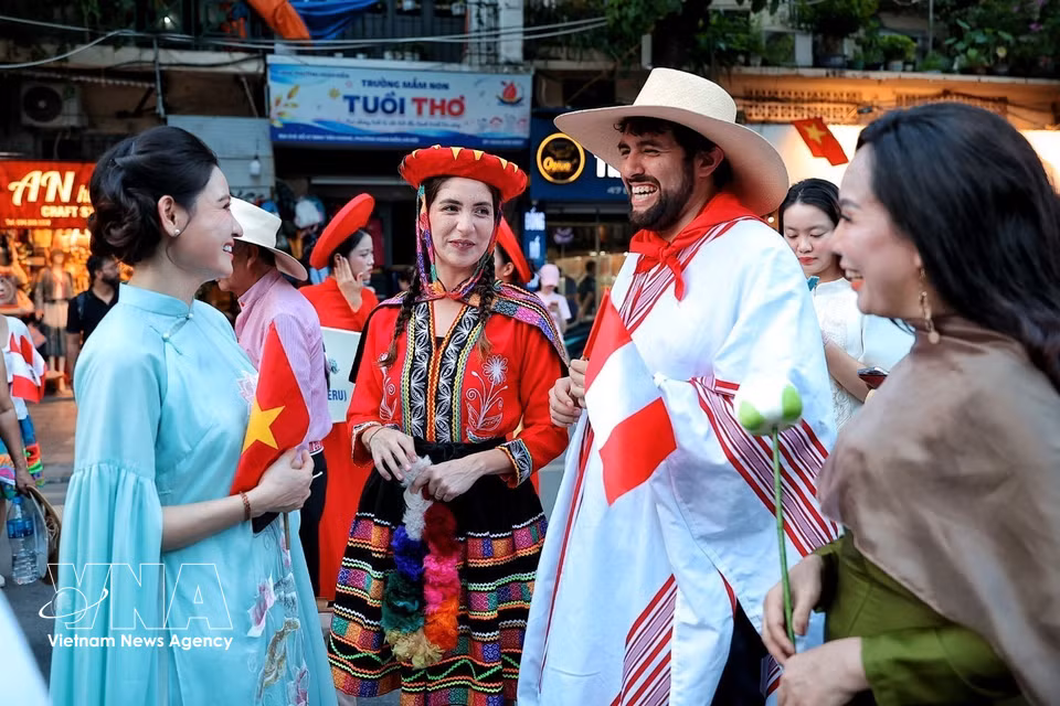 在参加“异彩五洲”街头艺术节巡游前，身着传统服饰的秘鲁代表团成员与河内妇女交流。图自越通社